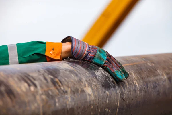 Oil worker\'s hand in green and orange work wear and suede gloves on oil deposit with a rusted drilling pipe at summer day.