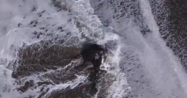 Batu Bolong sahilindeki kayaların üzerinden uçan dalgaların görüntüsü.