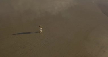 Gün batımında sahilde yürüyen genç bir kadının hava manzarası.