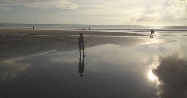 Luchtfoto van een jonge vrouw die bij zonsondergang aan het strand loopt — Stockvideo