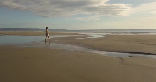 Vista aérea de una joven caminando por la playa al atardecer — Vídeos de Stock