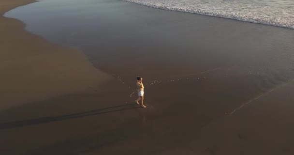 Letecký pohled na mladou ženu kráčející na pláži při západu slunce — Stock video