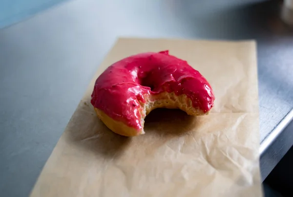 One Pink Glazed Vegan Donut with a Bite Taken Out of it