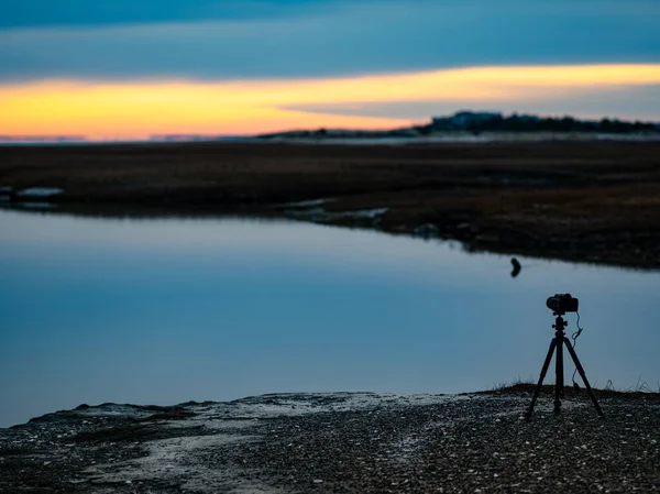 Et filmkamera på et stativ sidder alene på bredden af en flod - Stock-foto