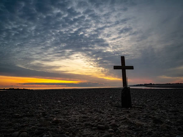 Una cruz solitaria en una playa rocosa al amanecer — Foto de Stock