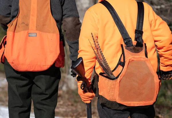 Dos cazadores caminando con escopetas y plumas de cola saliendo de su bolsa . — Foto de Stock