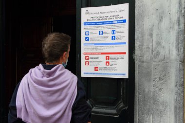 Pagani, Sa, İtalya - 17 Mayıs 2020: İnançlı bir genç adam, Basilica 'nın girişine yerleştirilen ve covid-19' un ikinci aşamasındaki güvenli erişim ve sosyal uzaklık kurallarını gösteren belirtileri okur.