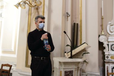Pagani, Sa, İtalya - 19 Mayıs 2020: Kilise rahibi Enzo, Kutsal Ayin 'in sona ermesinden sonra geçerli sayılan ürünler kullanılarak inananlara okunan mikrofonu sterilize etti .