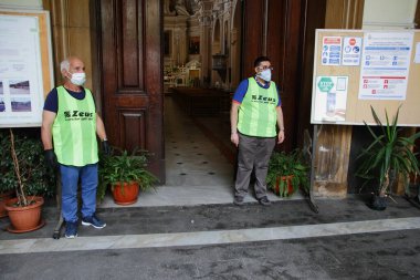 Pagani, Sa, İtalya - 19 Mayıs 2020: Kiliseye girmeden önce iki gönüllü, kilisedeki davranış kurallarını ve uyulması gereken tedbirleri açıklamak üzere müminleri karşıladı .