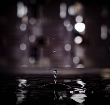 Durma hareketinin güzel, gizemli görüntüsü. Üç birleşik su damlası. İki damla daha koyu renkli, soyut bir bokeh damlası takip ediyor..