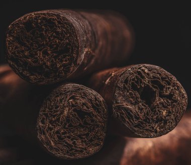 Üç erkeksi el sarması havana purosu sığ bir tarla derinliği ve koyu bir arka planı var..