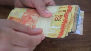 Salvador, Bahia / Brezilya - 28 Mart 2020: Brezilya 'da kullanılan para birimi olan Reais banknotları kadının ellerinde..