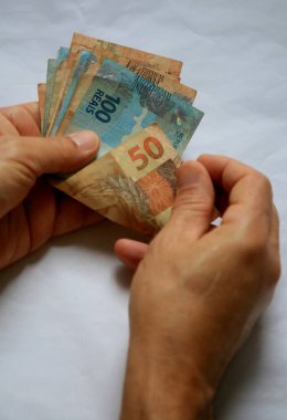 Salvador, Bahia / Brezilya - 28 Mart 2020: Brezilya 'da kullanılan para birimi olan Reais banknotları kadının elinde. * * * Yerel altyazı * *