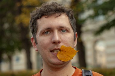 Dişinde sonbahar yaprağı olan genç adam..