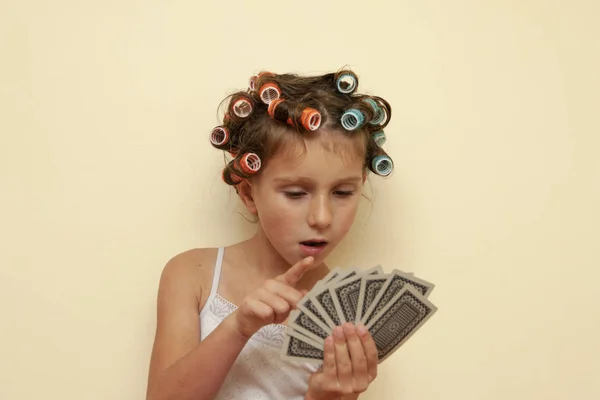 The little girl in hair rollers with game cards. The little girl is playing game cards.
