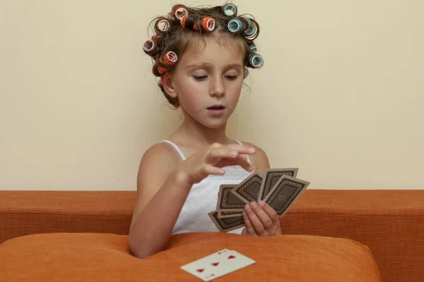 The little girl in hair rollers with game cards. The little girl is playing game cards.