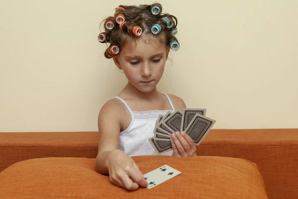 The little girl in hair rollers with game cards. The little girl is playing game cards.