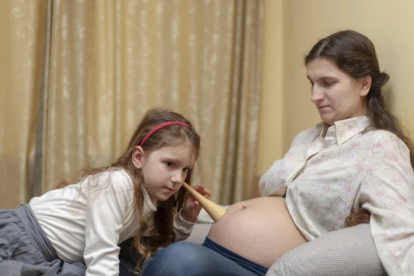 一个小女孩用听诊器检查她怀孕的妈妈的腹部 — 图库照片
