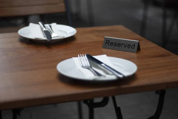 The served and reserved for two person table. Wooden table, shiny metal forks and knives, and white porcelain.
