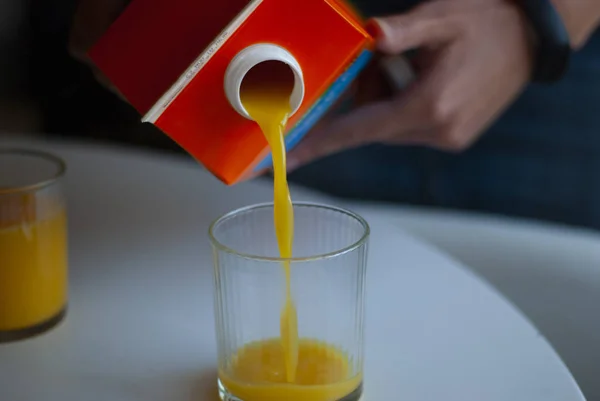 Orange juice is poured into a glass from a carton of juice.