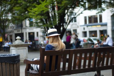 Parktaki bankta oturan güneş şapkalı kız. Arkadan bak..