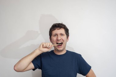 Adam beyaz arka planda dişlerini bambu diş fırçasıyla fırçalıyor.