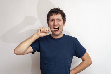 Adam beyaz arka planda dişlerini bambu diş fırçasıyla fırçalıyor.