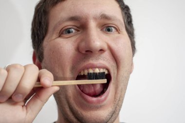 Adam beyaz arka planda dişlerini bambu diş fırçasıyla fırçalıyor.