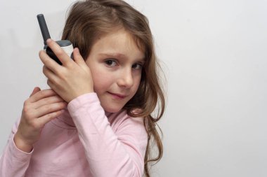 The little girl listens to a walkie-talkie on a white background isolated. Concept of communication, speaking, information.