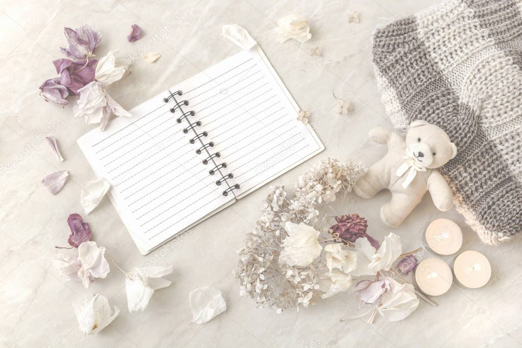 toy bear, dried flowers, sweater, notebook and candles on a ligh