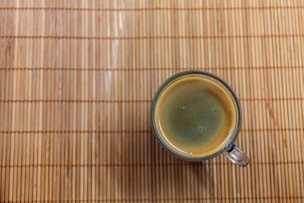 Espresso coffee with golden fine-bubbled crema seen from above in a crystal clear cup on bamboo plate holder. — Stock Photo, Image