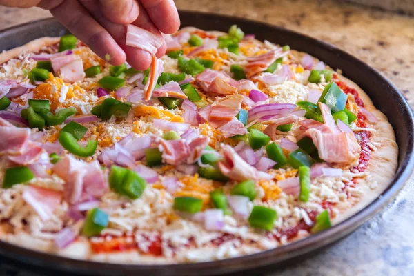 Így, pizzát. Szakácsok keze hinti szalonnával és a paprika. Amerikai stílusú, főzés-sütés-csészébe — Stock Fotó