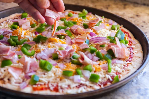 Haciendo pizza. Cocina mano espolvorea tocino y pimiento. Estilo americano, cocinar en una bandeja para hornear — Foto de Stock