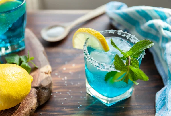 Koktajl alkoholowy na drewnianym stole otoczony składnikami takimi jak cytryna, sól, cukier, lód — Zdjęcie stockowe