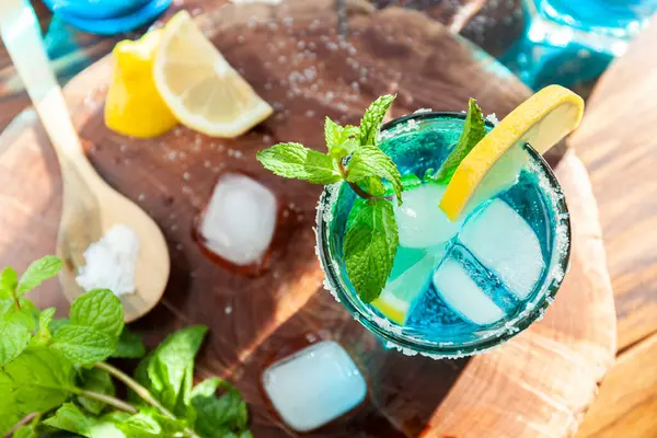 Alkoholischer Cocktail auf einem Holztisch, umgeben von Zutaten wie Zitrone, Salz, Zucker, Eis — Stockfoto