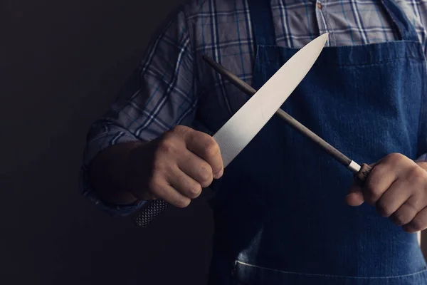 Man kock händer slipning kniv med slipstav. Mörk bakgrund. Låg nyckel — Stockfoto