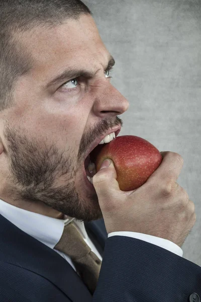 Angry businessman eating an apple — Stock Photo, Image