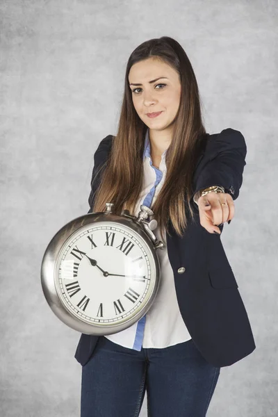 Happy business woman holding a clock and pointing at you — Stock Photo, Image