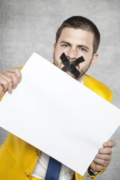 Hombre de negocios con cinta adhesiva en la boca, sosteniendo una tarjeta en blanco — Foto de Stock