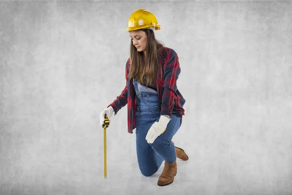 Женщина-строитель на коленях, метр в руке — стоковое фото