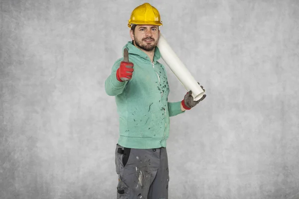 Um trabalhador sério com planos de construção na mão, polegar para cima — Fotografia de Stock