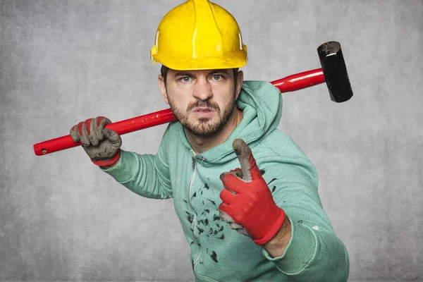 Um trabalhador com um martelo grande ameaça seu dedo — Fotografia de Stock