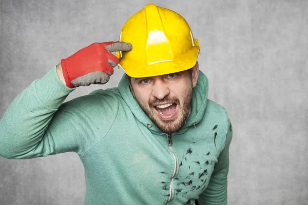A mad disgruntled worker peeking in a protective helmet — Stock Photo, Image