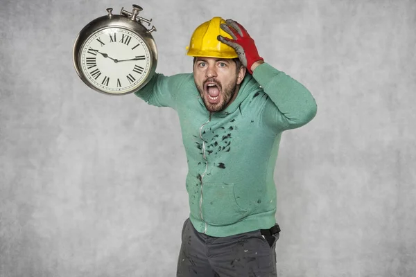 Förvånad över arbetare håller en klocka i sin hand, tar tag i hans huvud — Stockfoto