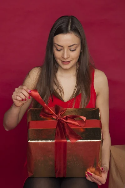 Jovem mulher em um vestido vermelho abre um presente — Fotografia de Stock