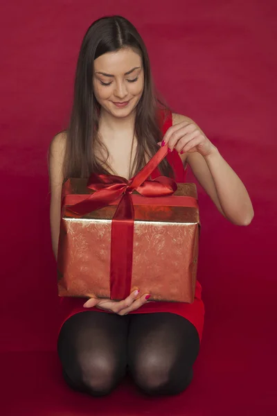 Mulher em um vestido vermelho abre um presente — Fotografia de Stock
