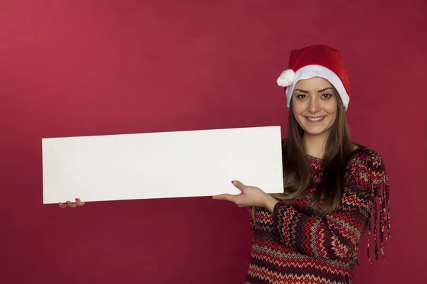 Menina bonito usando um chapéu de Natal em um fundo vermelho segurando um — Fotografia de Stock