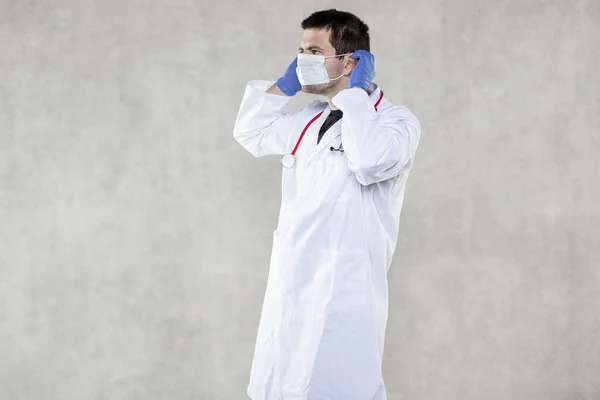 a doctor in protective clothing shows how to put on a protective mas