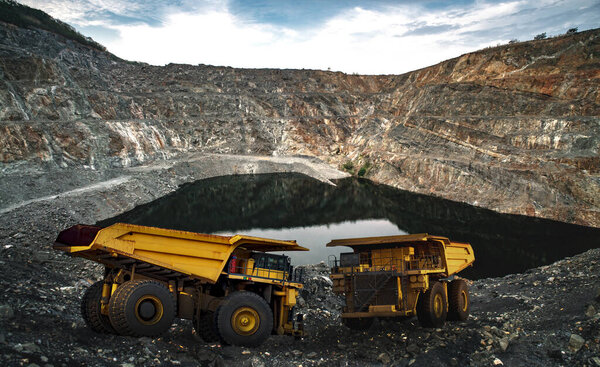 Yellow dump truck loading minerals copper, silver, gold, and other  at mining quarry.