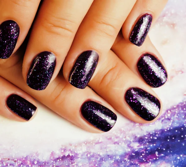 manicure stylish concept: woman fingers with nails purple glitter on nails like cosmos, universe background